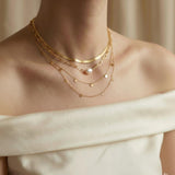 A model wearing a layered Caellia 18K gold necklace set featuring a baroque pearl and coin charms.