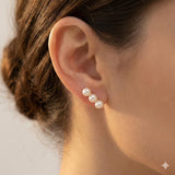 A close-up of a person wearing Caellia 14K gold plated freshwater pearl crawler earrings.