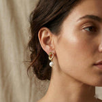 A woman wears Caellia 14K gold knot earrings featuring a dangling freshwater pearl.