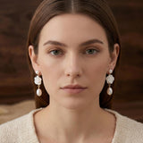 A woman wears Caellia 14K gold camellia flower earrings with dangling freshwater pearls.