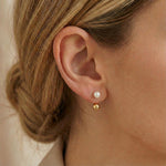 A close-up of a person wearing Caellia 14K gold double-sided freshwater pearl stud earrings.