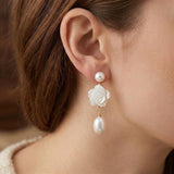 A model wears Caellia 14K gold dangle earrings featuring a camellia flower and freshwater pearl.