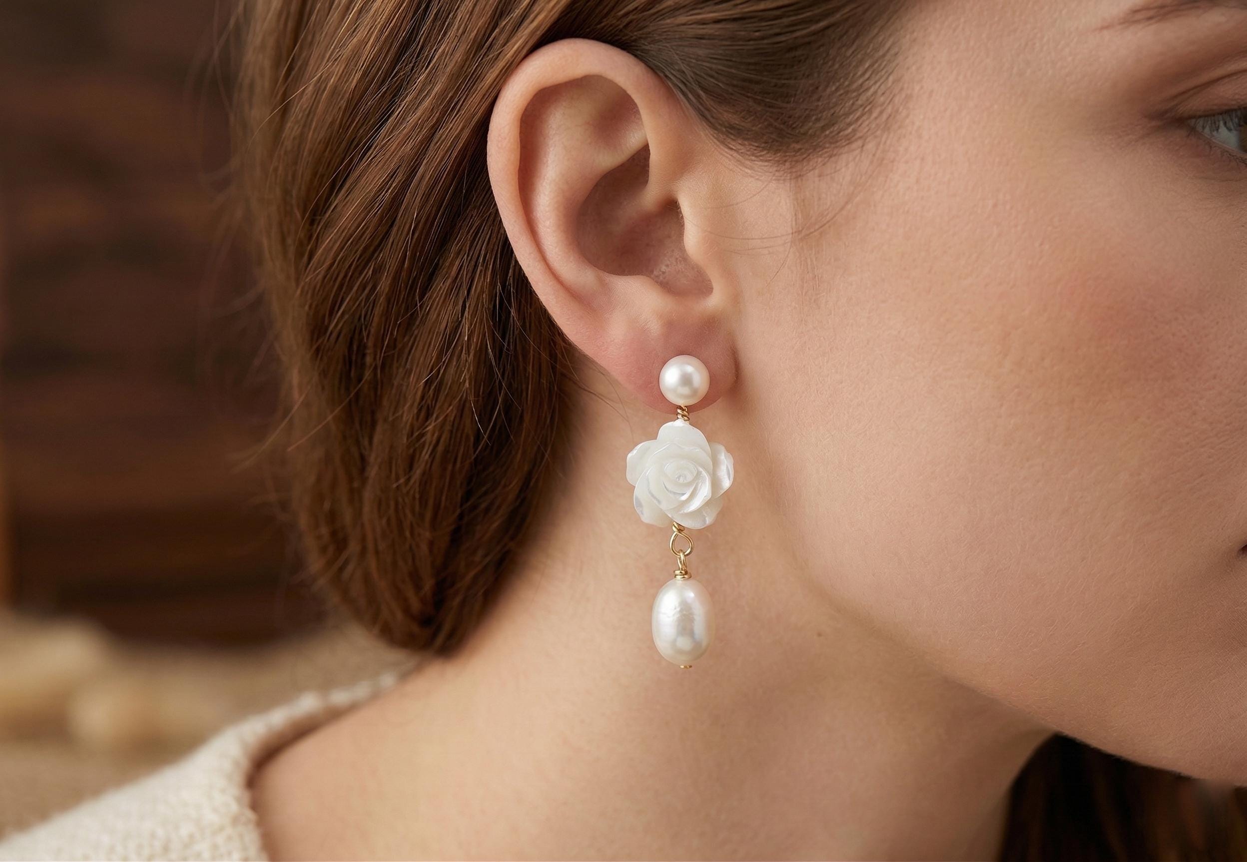 A model wears Caellia 14K gold dangle earrings featuring a camellia flower and freshwater pearl.