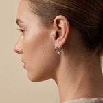 A model wearing Caellia sterling silver heart-shaped huggie hoop earrings with freshwater pearls.