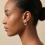 A model wearing Caellia sterling silver heart huggie hoop earrings with a freshwater pearl.