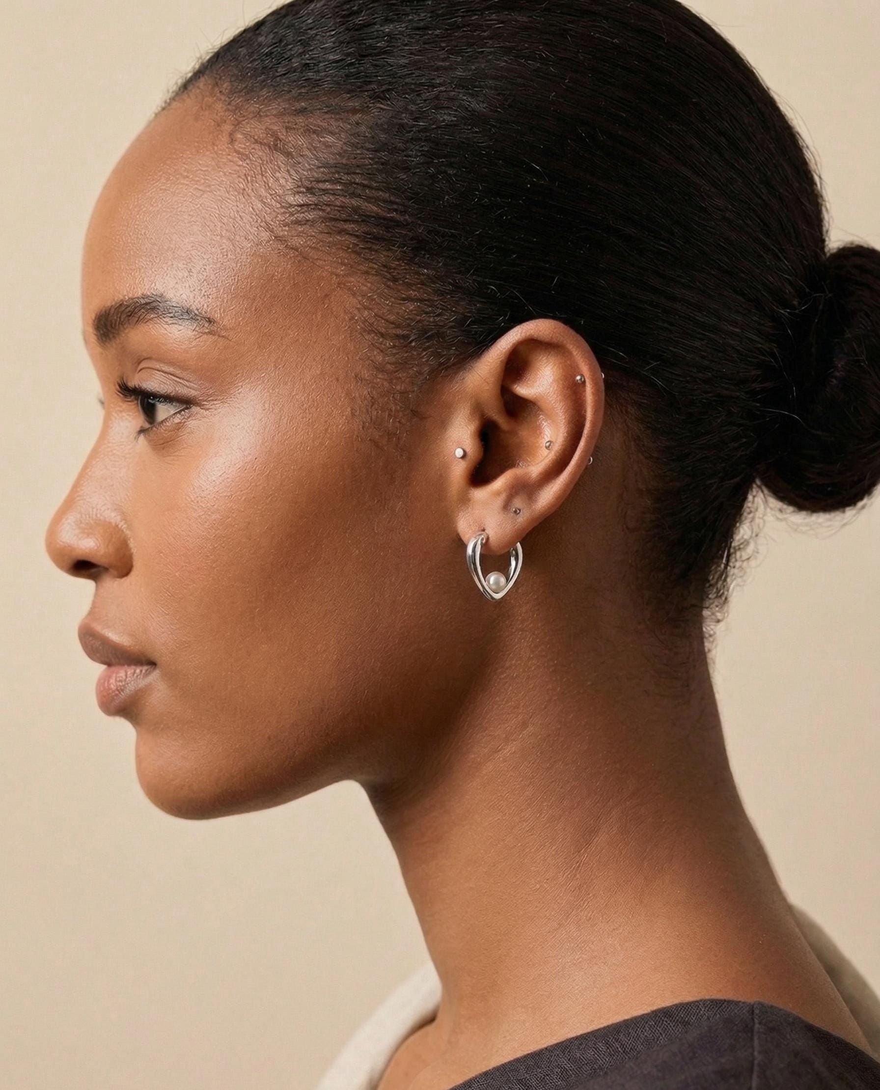 A model wearing Caellia sterling silver heart huggie hoop earrings with a freshwater pearl.