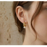 A model wears Caellia 14K gold vintage huggie hoop earrings featuring a small freshwater pearl.