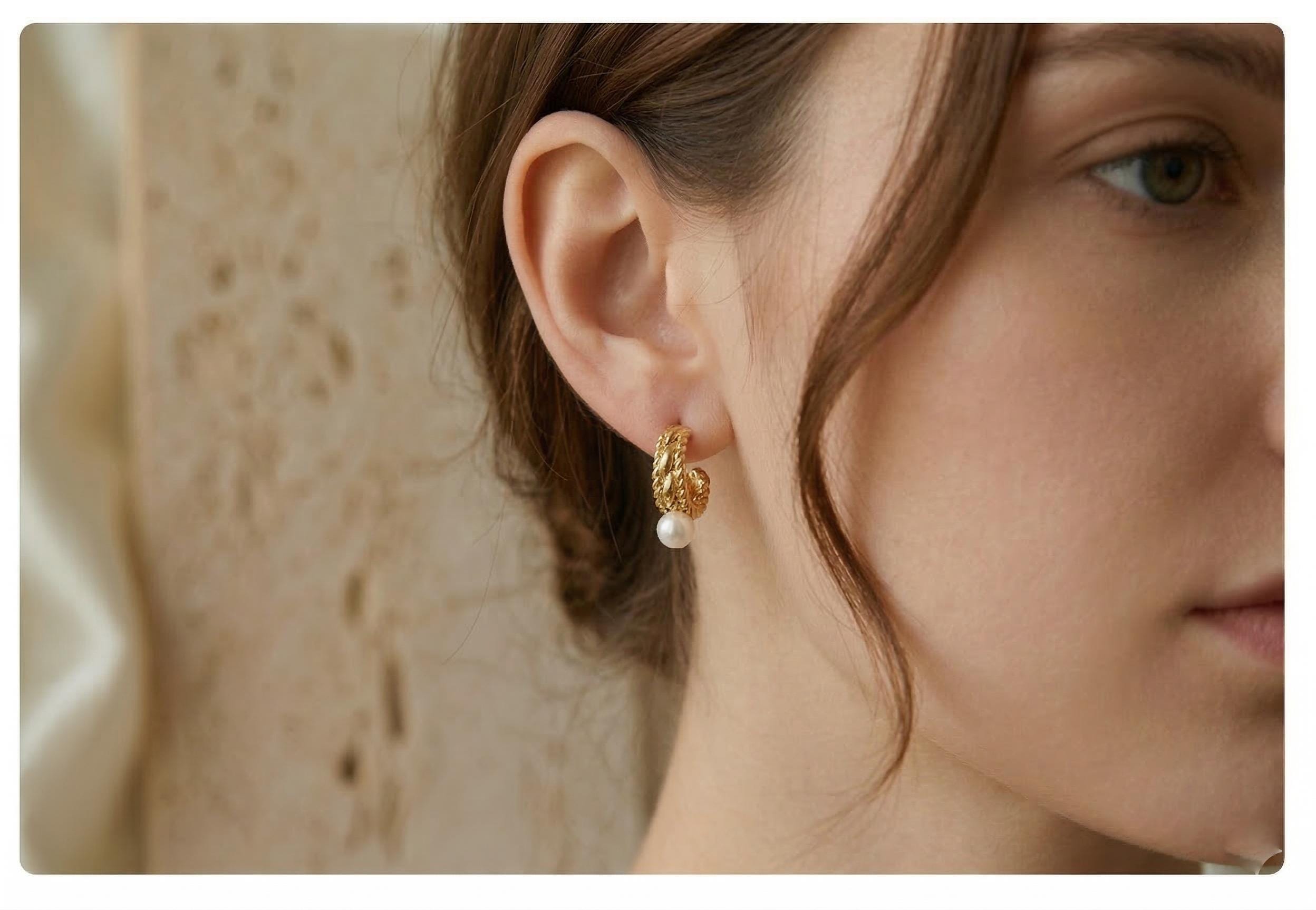 A model wears Caellia 14K gold vintage huggie hoop earrings featuring a small freshwater pearl.