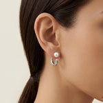 A model wears Caellia freshwater pearl hoop earrings featuring a lustrous pearl on a silver hoop.