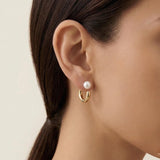 A close-up of a model wearing Caellia 14K gold hoop earrings featuring a freshwater pearl stud.