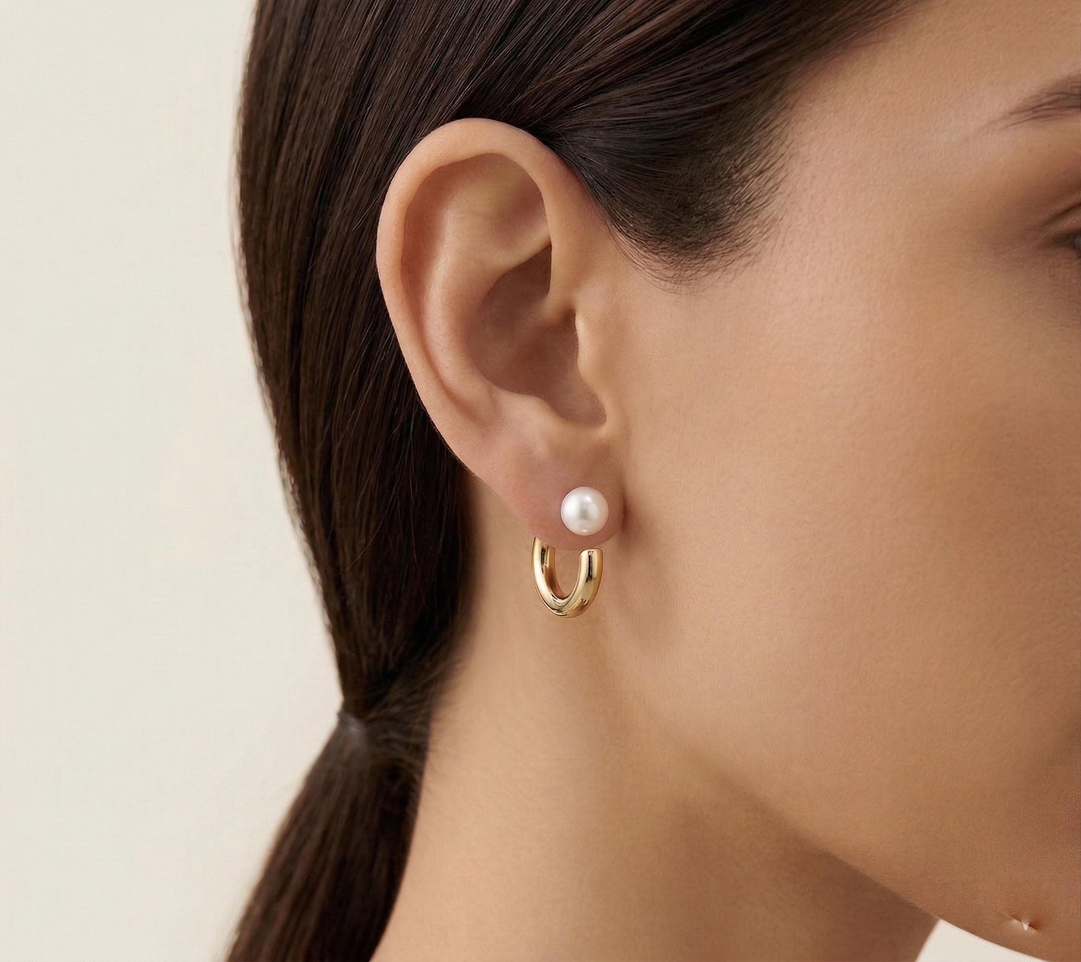 A close-up of a model wearing Caellia 14K gold hoop earrings featuring a freshwater pearl stud.