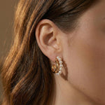 A close-up of a person wearing Caellia 14K gold-filled hoop earrings accented with small pearls.
