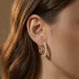 A close-up of a person wearing Caellia 14K gold-filled hoop earrings accented with small pearls.
