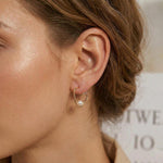 A model wears Caellia rose gold heart-shaped hoop earrings featuring a single freshwater pearl.