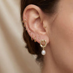 Close-up of gold rose pearl drop stud earring worn with a delicate ear stack