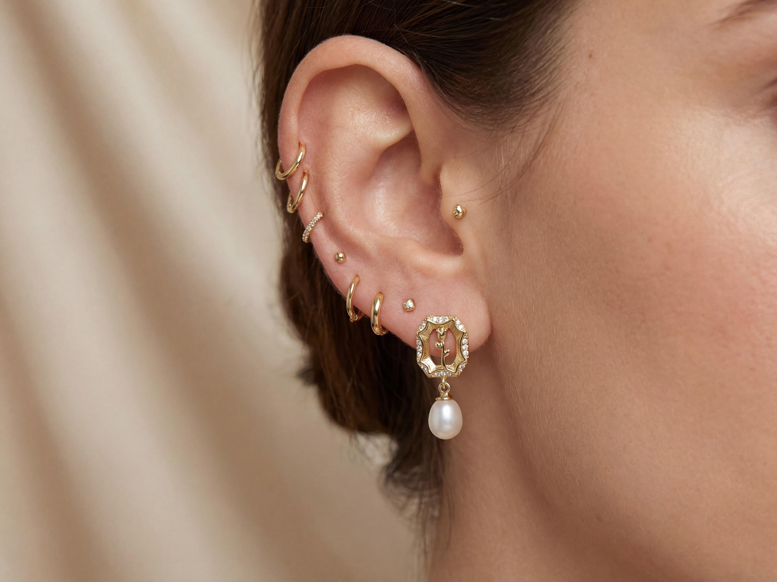 Close-up of gold rose pearl drop stud earring worn with a delicate ear stack