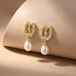 Gold rose freshwater pearl earrings displayed on a curved beige backdrop