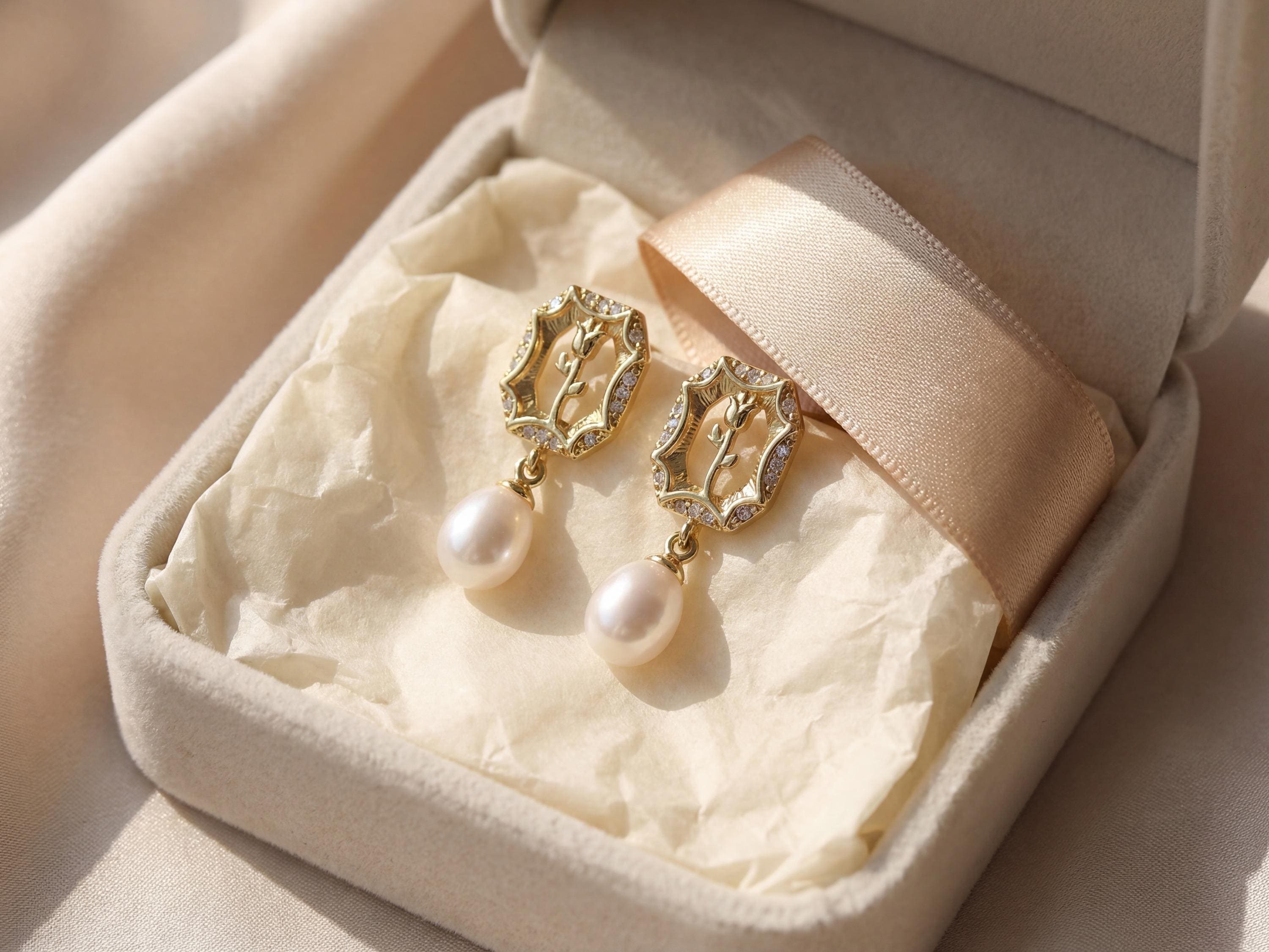 Gold rose pearl drop earrings presented inside a cream jewelry box