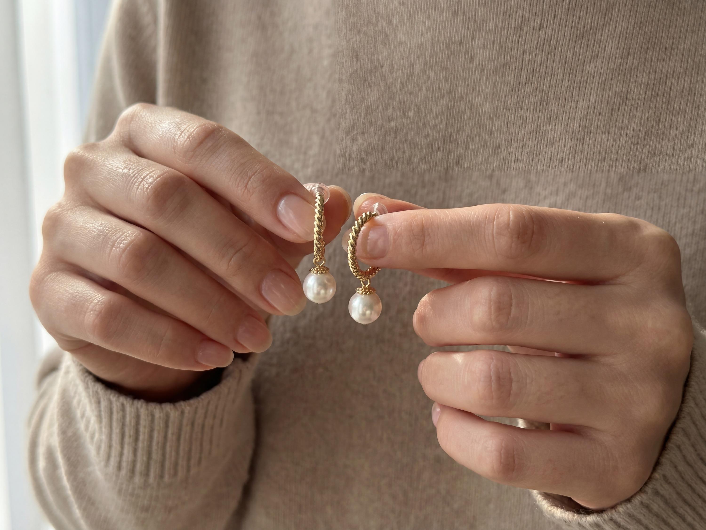 Hands holding a pair of gold half hoop earrings with round white freshwater pearls