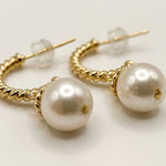 Macro view of white freshwater pearls and twisted gold plated half hoop earring details