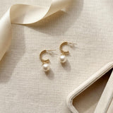 Gold half hoop freshwater pearl earrings arranged beside ribbon and a jewelry box