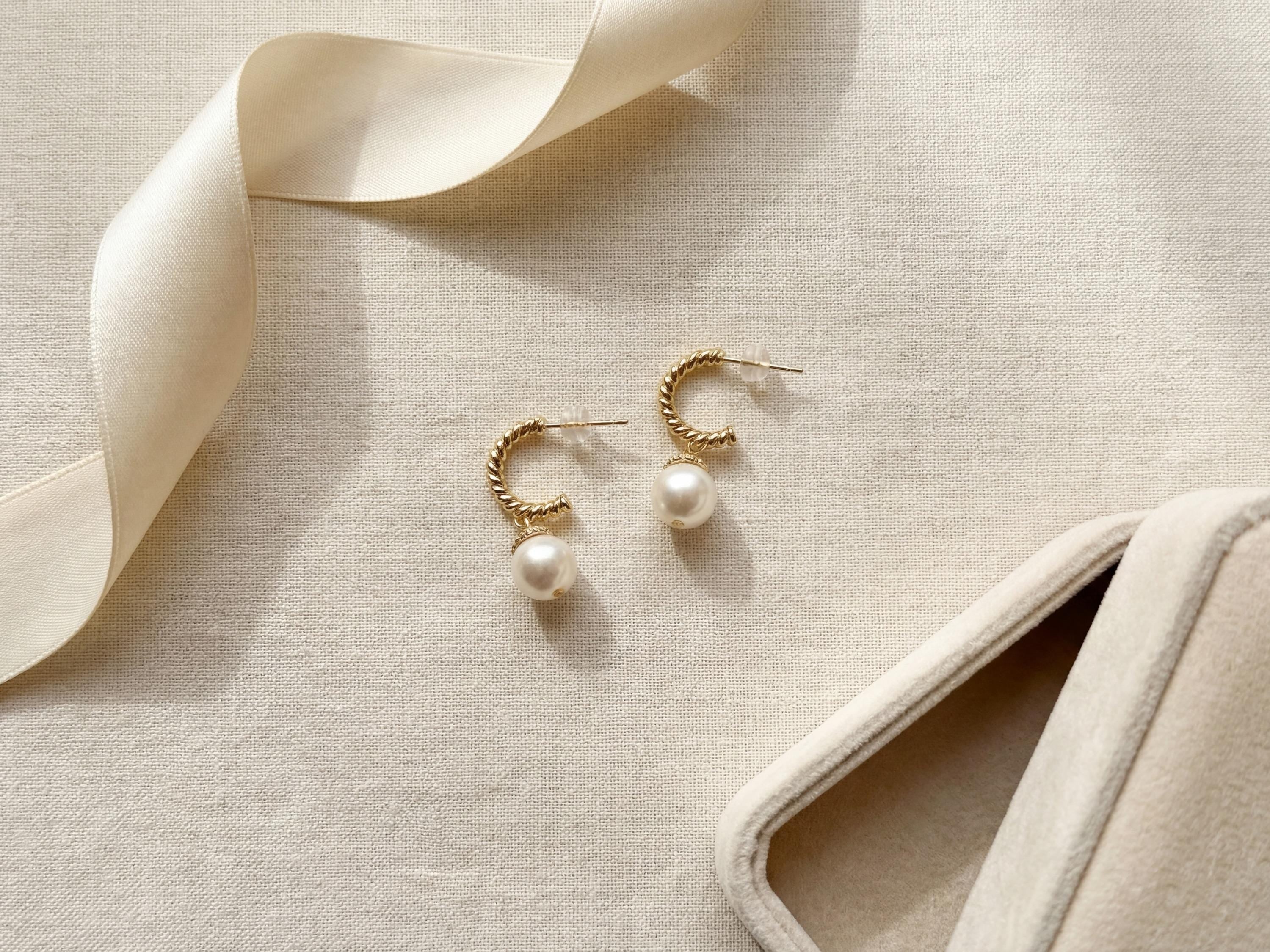 Gold half hoop freshwater pearl earrings arranged beside ribbon and a jewelry box