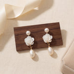 White floral pearl earrings displayed on wood with gift box beside them