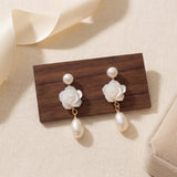 White floral pearl earrings displayed on wood with gift box beside them