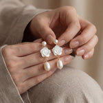 Hands holding a pair of white camellia flower pearl drop earrings