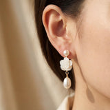 White camellia flower pearl dangle earring worn on ear with gold plated details