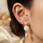 Close on-ear view of white floral pearl dangle earring with gold details