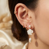 Close on-ear view of white floral pearl dangle earring with gold details