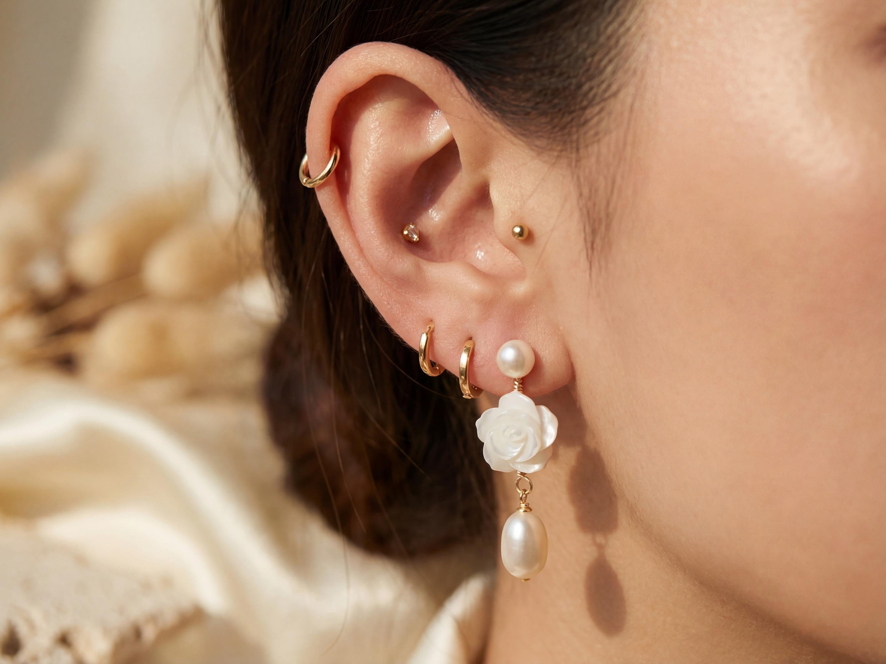 Close on-ear view of white floral pearl dangle earring with gold details
