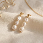 Pair of gold plated triple freshwater pearl drop earrings on soft linen with delicate dried flowers