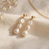 Pair of gold plated triple freshwater pearl drop earrings on soft linen with delicate dried flowers