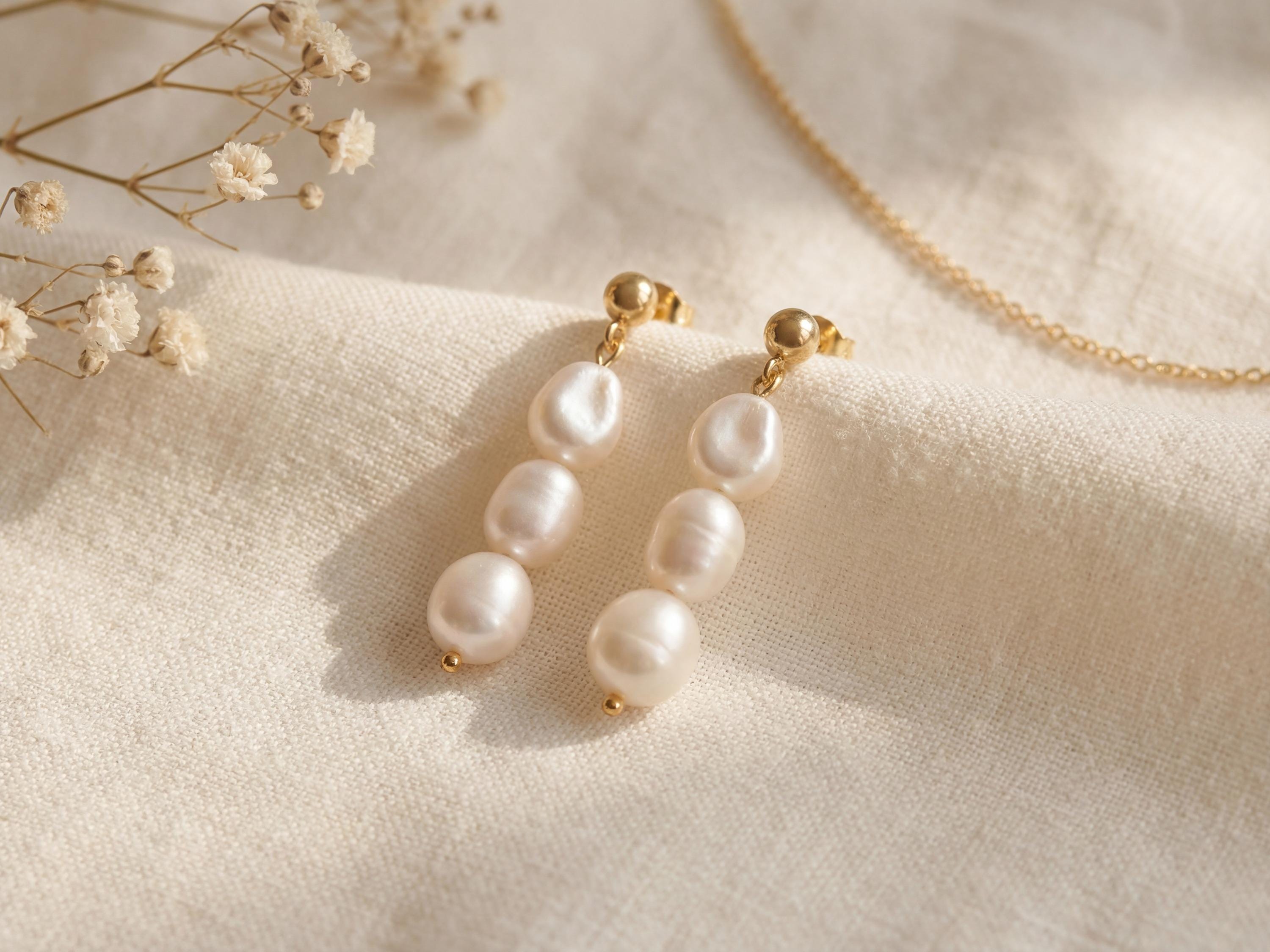 Pair of gold plated triple freshwater pearl drop earrings on soft linen with delicate dried flowers