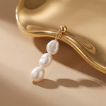 Close-up of one gold plated triple freshwater pearl drop earring styled against a sculptural gold surface