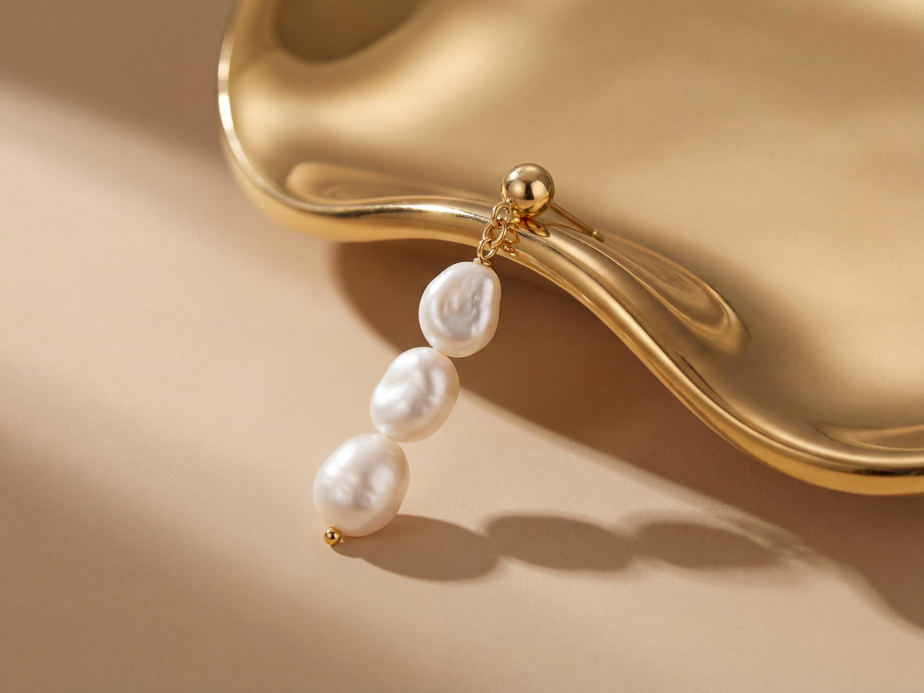 Close-up of one gold plated triple freshwater pearl drop earring styled against a sculptural gold surface