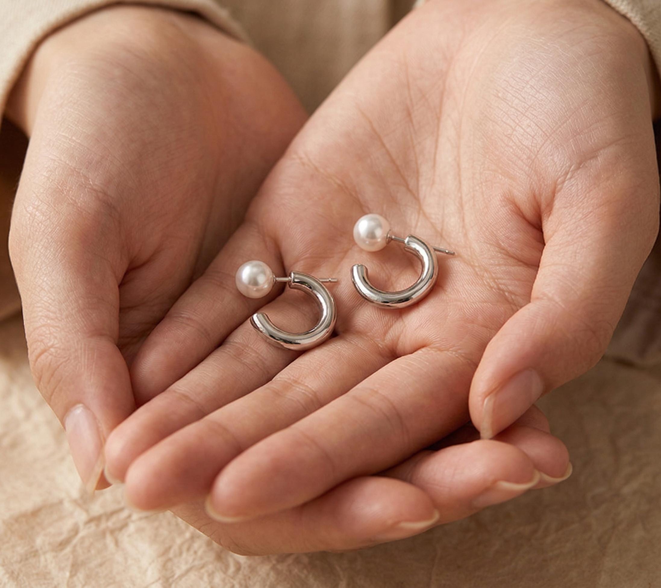 A pair of Caellia freshwater pearl hoop earrings resting in a person's cupped hands.