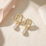 Gold rose pearl drop earrings styled on fabric with a soft pink ribbon