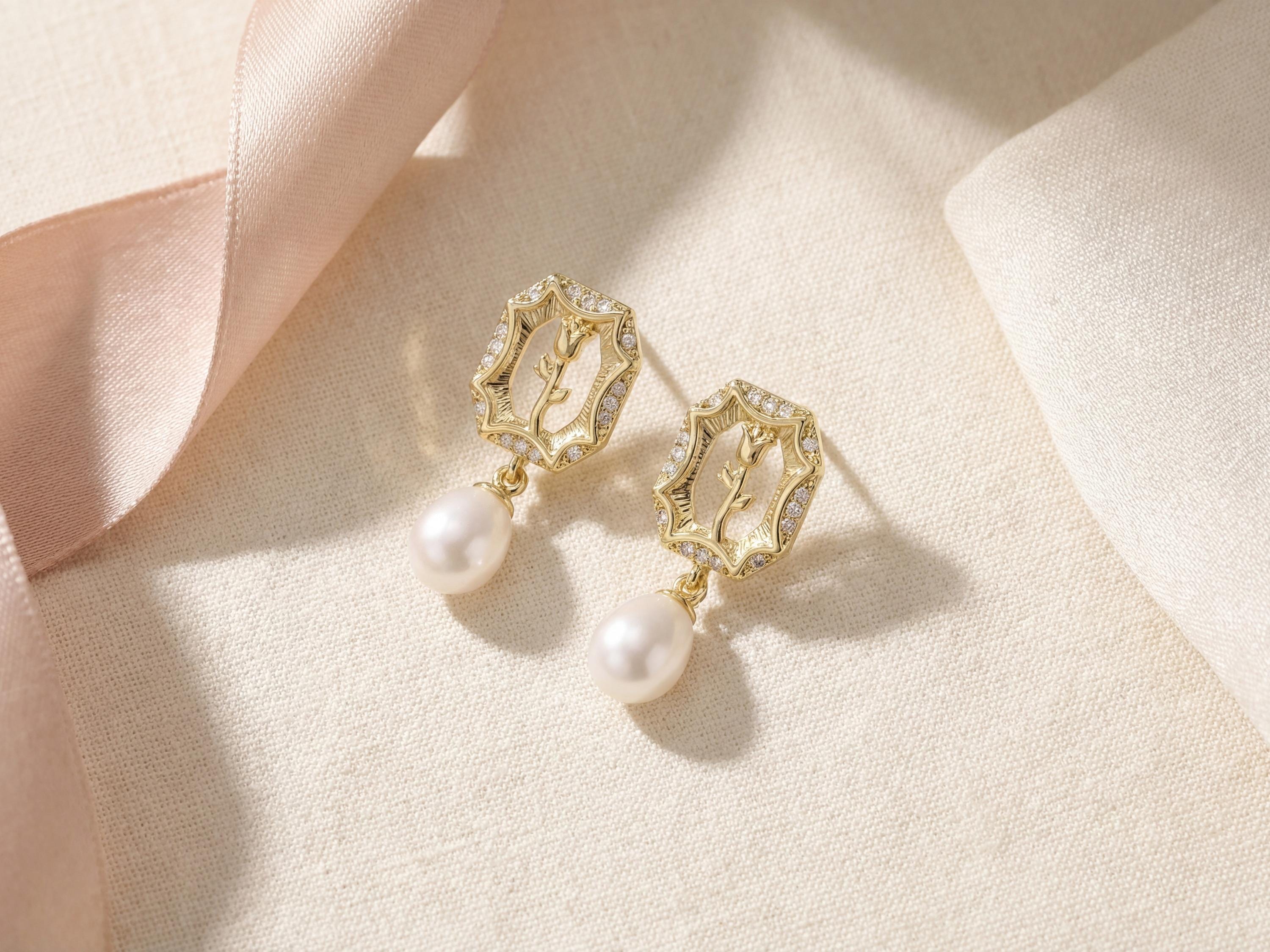 Gold rose pearl drop earrings styled on fabric with a soft pink ribbon