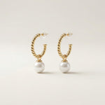 Pair of twisted gold half hoop pearl earrings with clear push backs on a neutral background