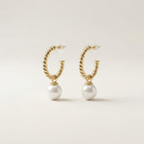 Pair of twisted gold half hoop pearl earrings with clear push backs on a neutral background