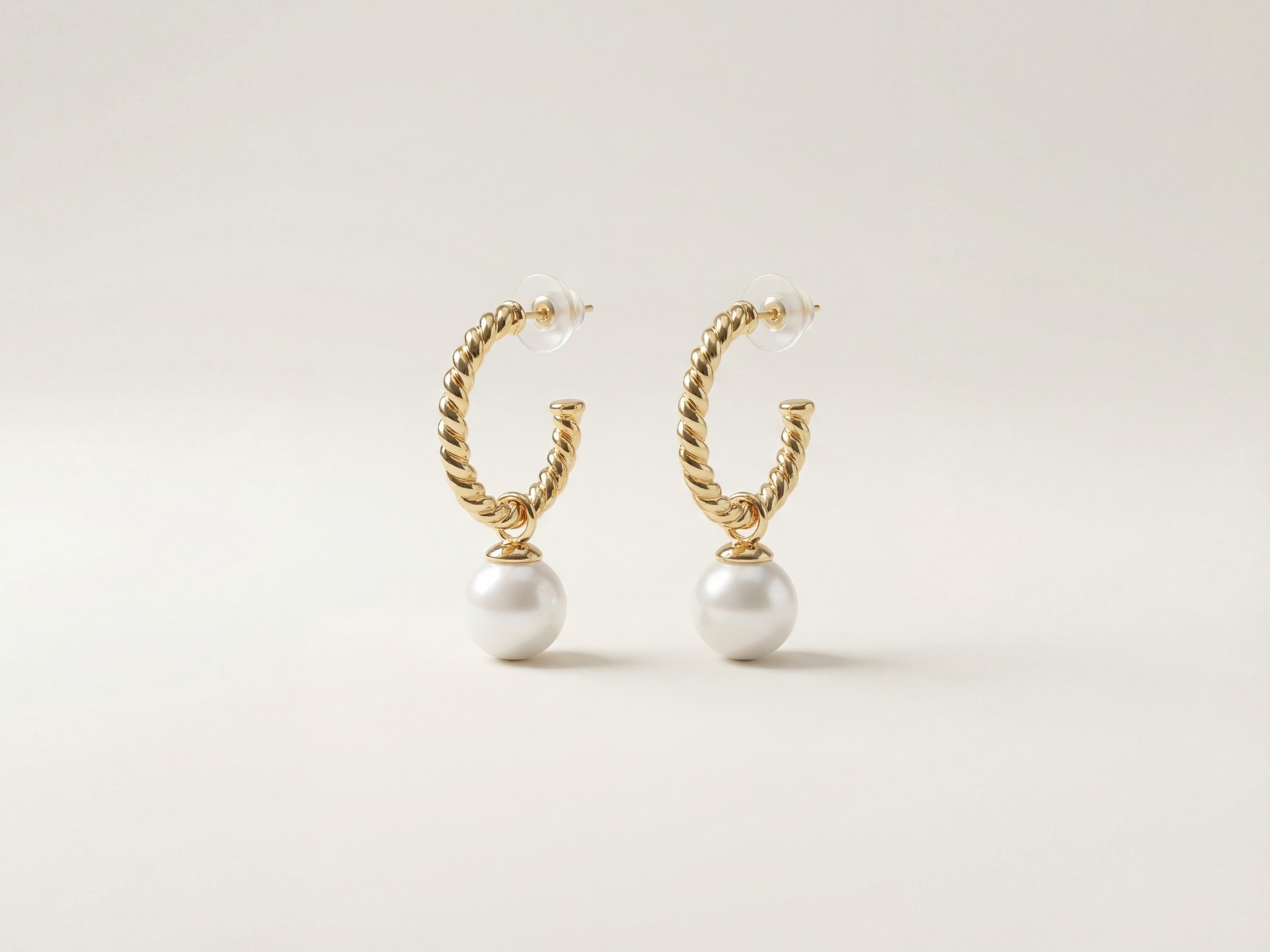 Pair of twisted gold half hoop pearl earrings with clear push backs on a neutral background