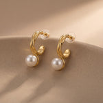 Pair of curved gold and white pearl earrings displayed on a neutral ceramic surface
