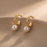 Pair of curved gold and white pearl earrings displayed on a neutral ceramic surface