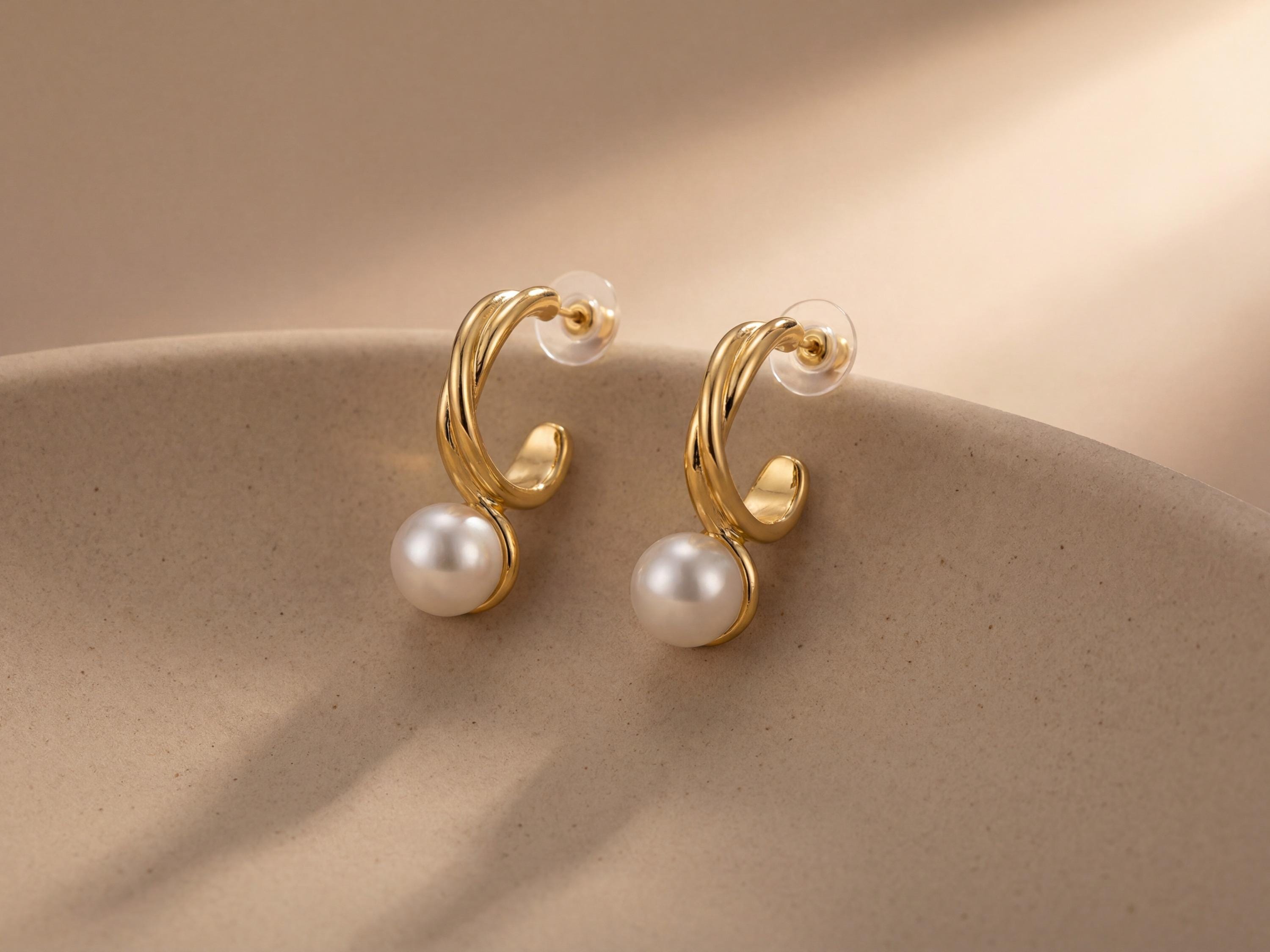 Pair of curved gold and white pearl earrings displayed on a neutral ceramic surface