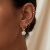 Gold half hoop pearl drop earring worn with a minimalist ear stack