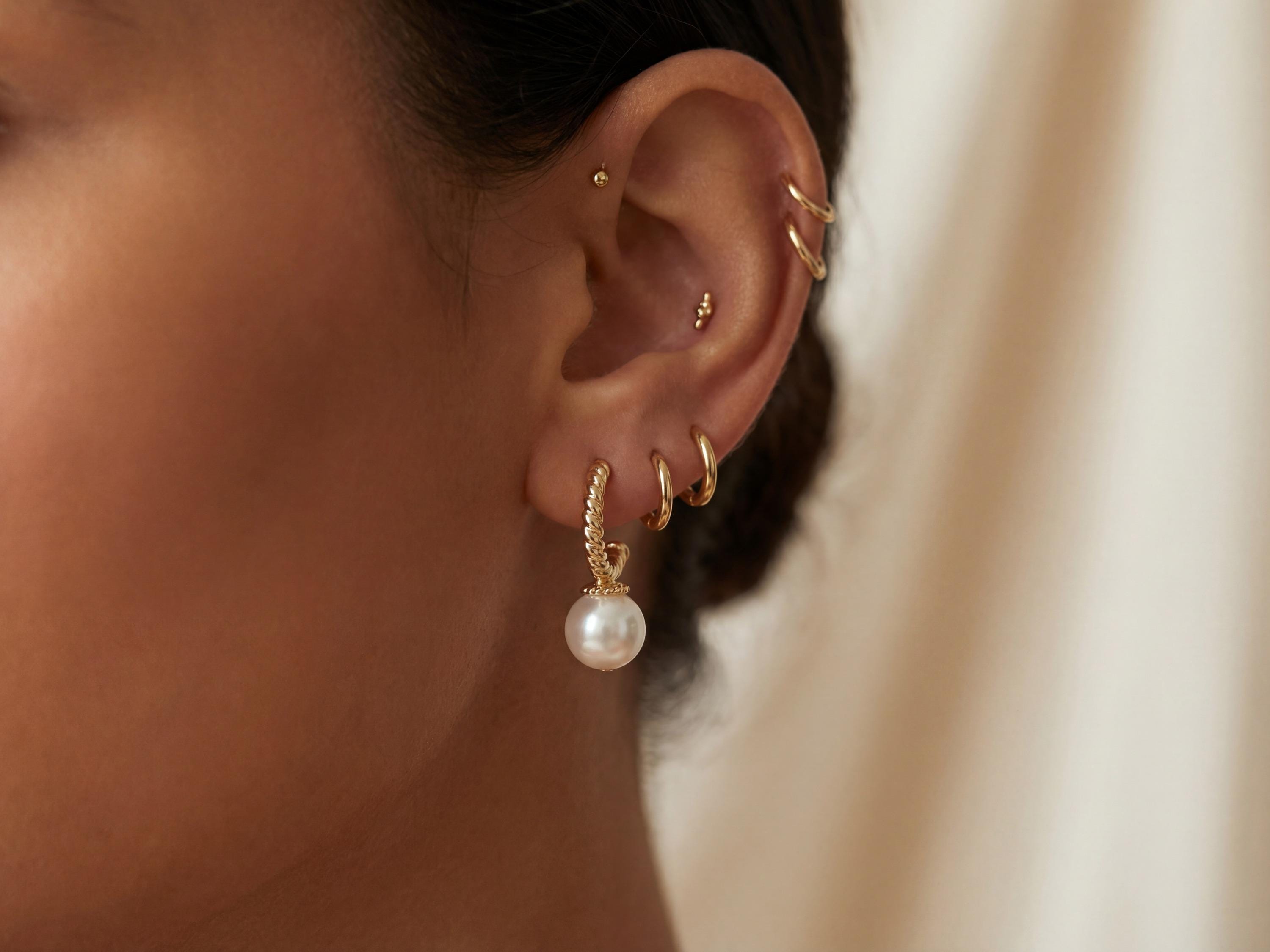 Gold half hoop pearl drop earring worn with a minimalist ear stack