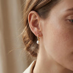 Model wearing a small gold half hoop earring with a white freshwater pearl drop